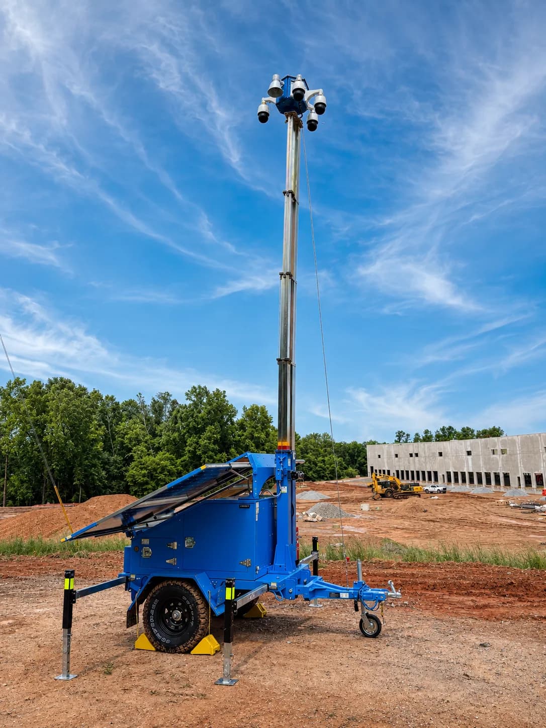 A blue solar-powered mobile surveillance trailer with its camera mast raised, deployed on a construction site