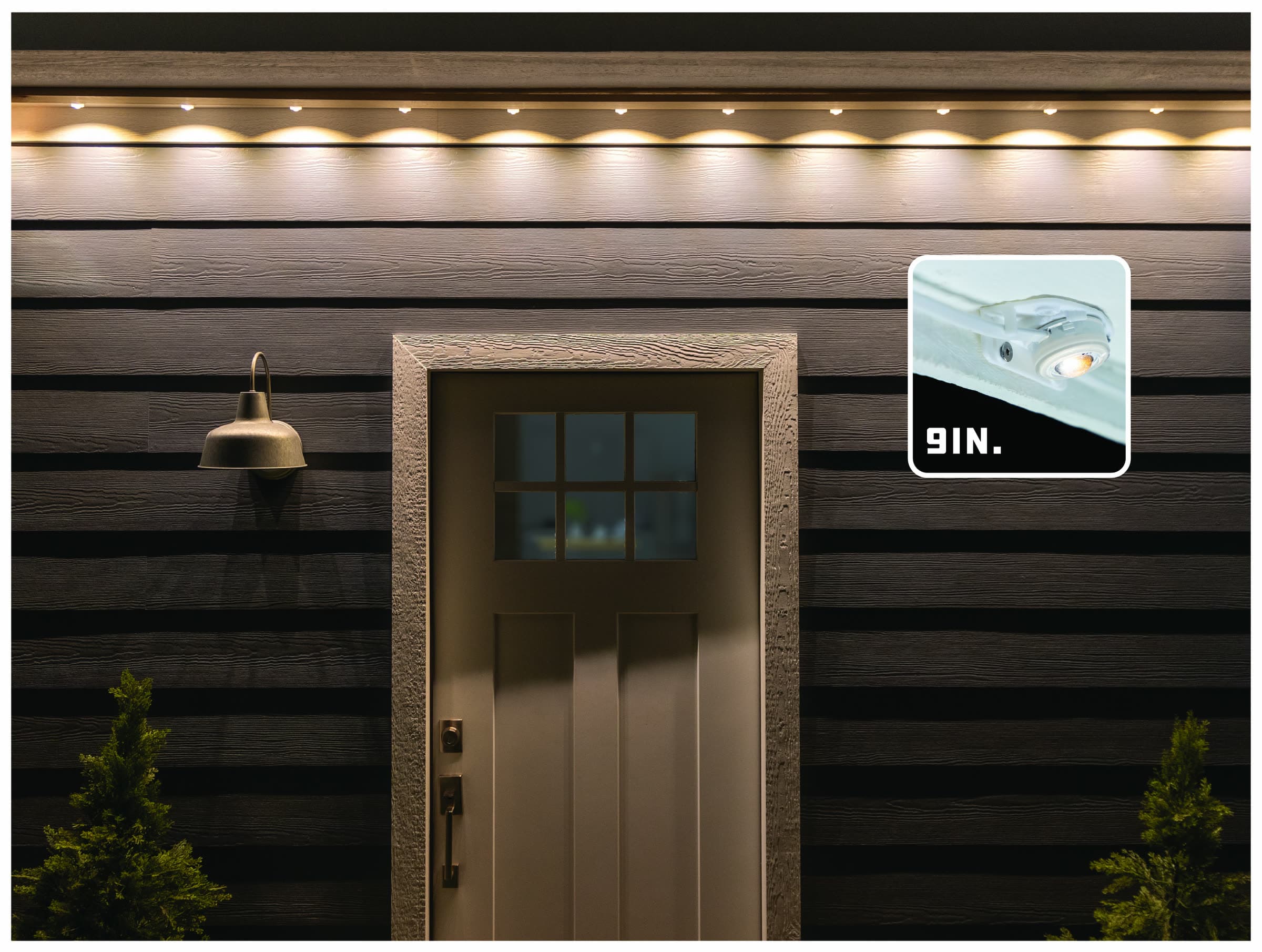 A lit entry door photographed at night with the under-eave lights mounted at a 9 inch setback, producing a tight, bright band of light close under the eave