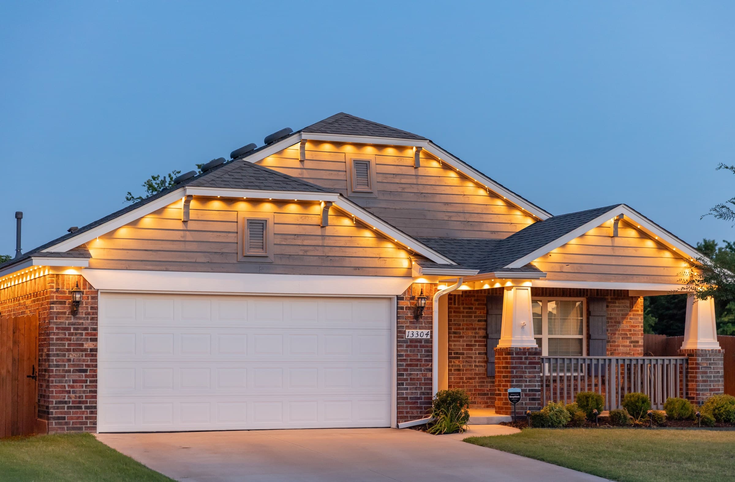 A single-story brick home at dusk with a warm-white under-eave line running the full roofline and gables
